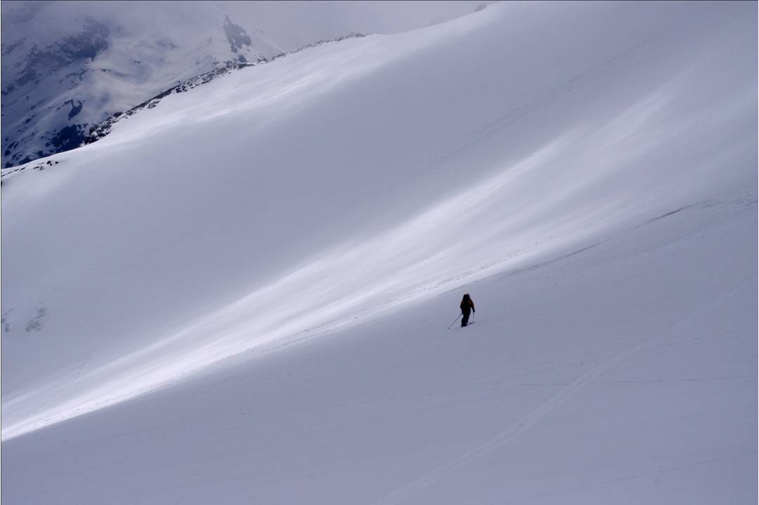 Nuages protecteurs : La descente emprunte toute la largeur du glacier des Plattes. Les nuages jouent à plein un effet de protection du manteau neigeux en limitant l'exposition, sans affaiblir la visibilité à skis. Le rêve.