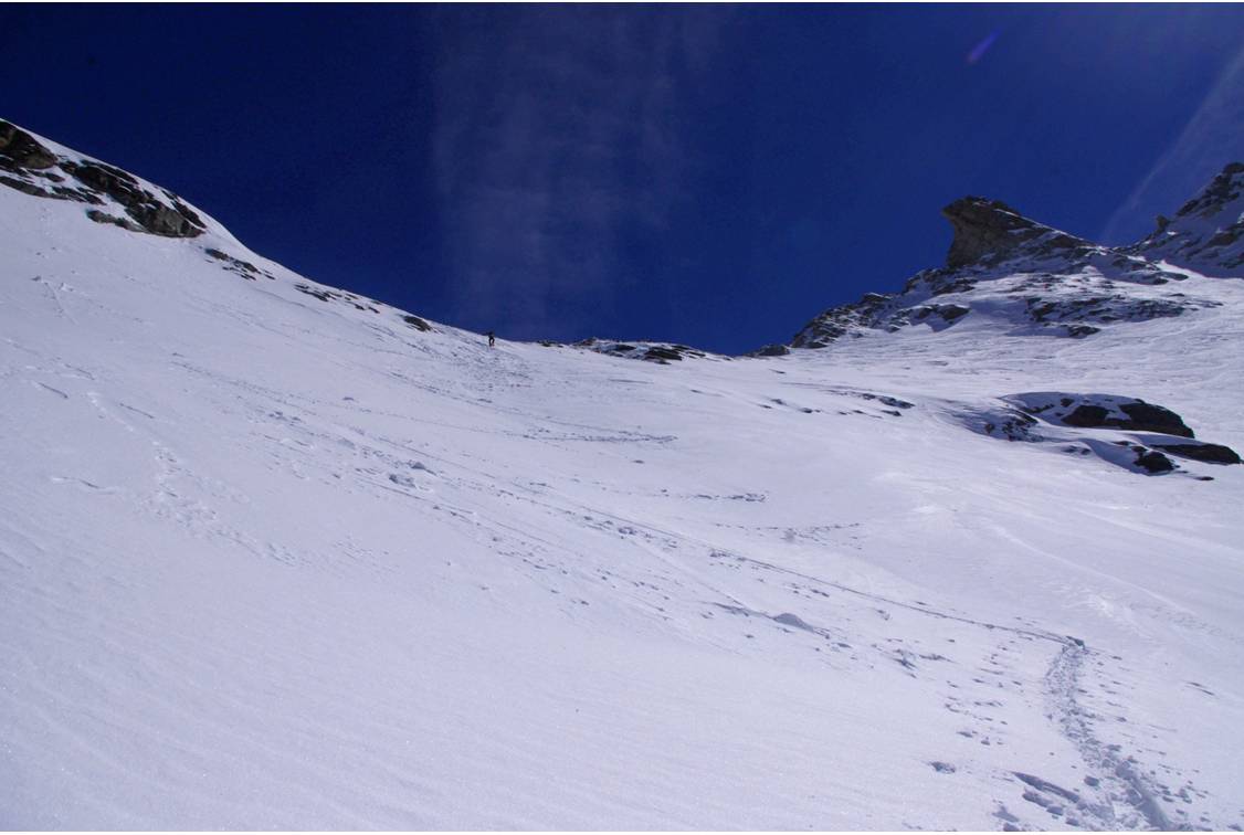 #23 Sous le Col 3513 : Passage de Nicola en mode skis sur le sac. Le col au centre des Rousses N et S, forme son incurvation au dessus de nos têtes. Sous le Col 3513 : Passage de Nicola en mode skis sur le sac. Le col au centre des Rousses N et S, forme son incurvation au dessus de nos têtes.