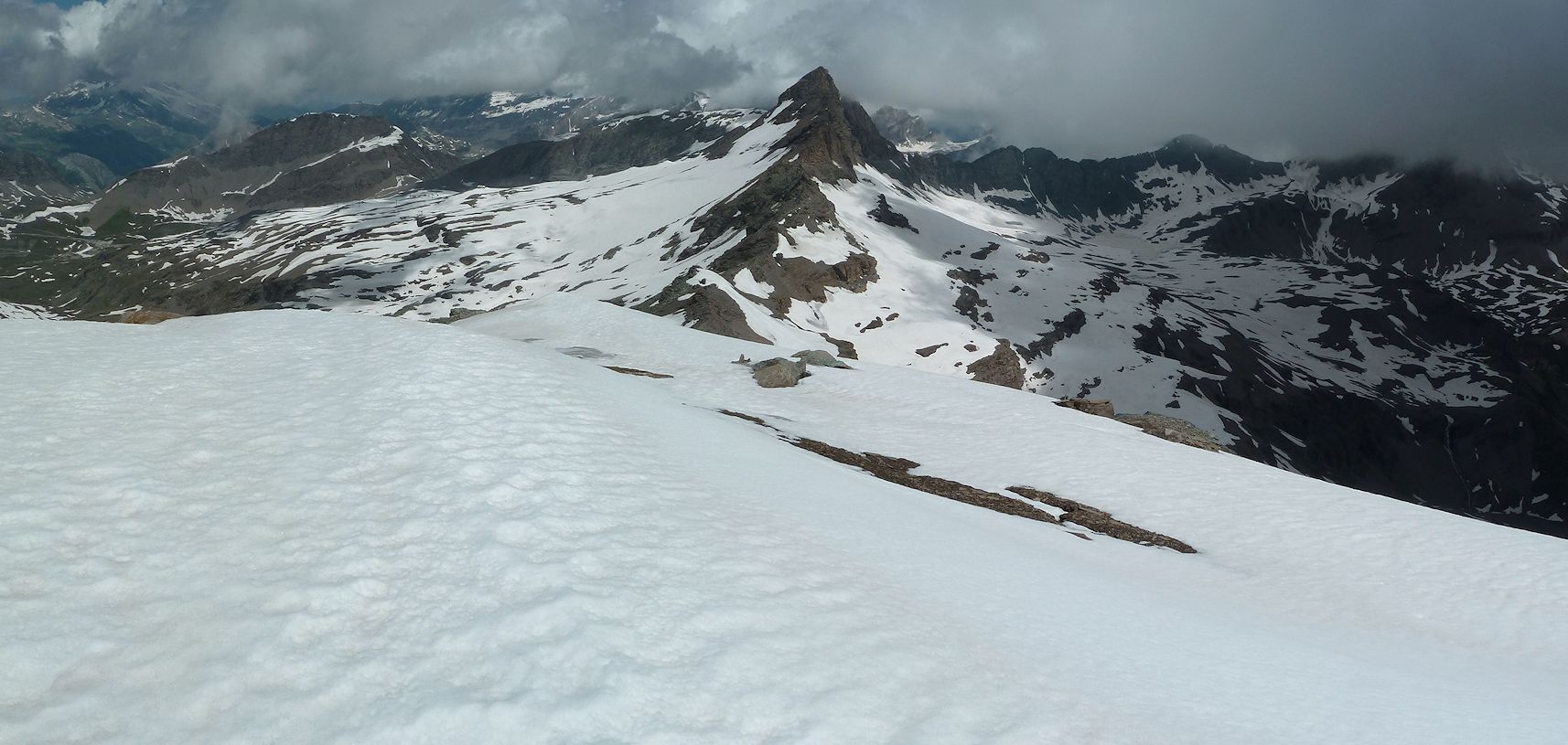 Depuis l'Ouille Noire : vue panoramique vers le Nord sur le versant Pisaillas et le versant Montet. La pointe du Montet au centre de la photo. Les Aiguilles Rousse, à droite, dans le nuage